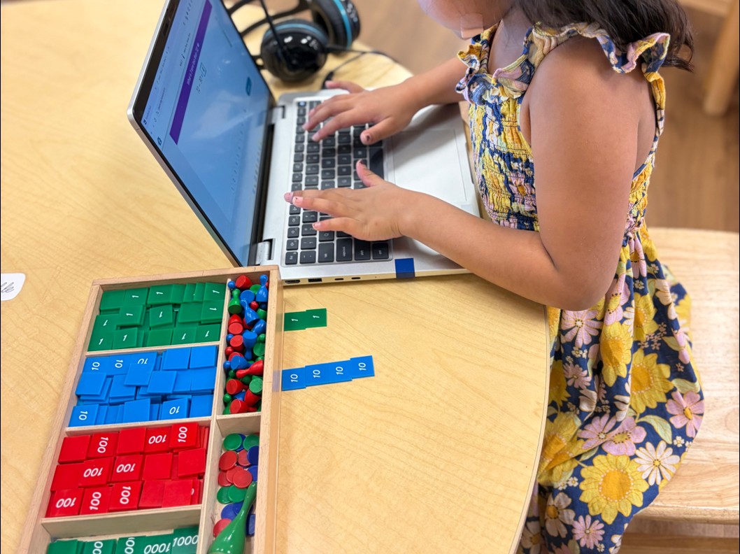 Student learning on laptop alongside Montessori math stamp game materials