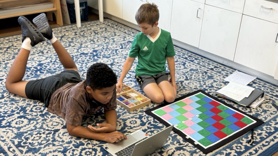 Students working with laptop and Montessori checkerboard on the floor