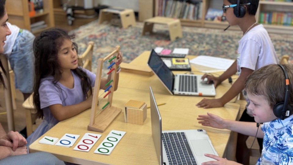 Students using laptops with Montessori math materials at a group table