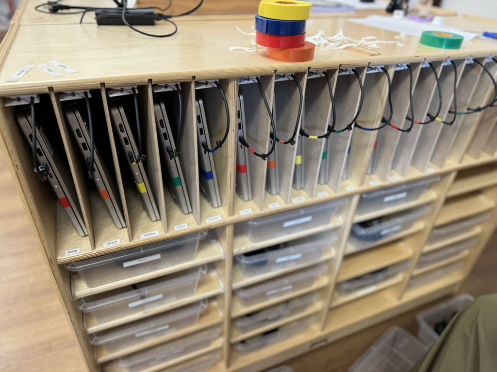 Student laptops organized on Montessori shelves with labeled slots